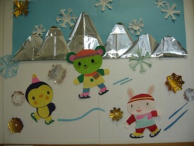 切り紙による壁面装飾です。ペンギンとクマとウサギの子どもがスケートをしています。遠くには山々が見えます。雪の結晶がまっています。