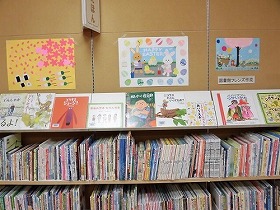 山田駅前図書館絵本コーナーの壁飾り。満開のサクラの下でお花見をしている動物たちの絵や赤、青、緑と色とりどりのイースターエッグで彩られた絵が飾られています。