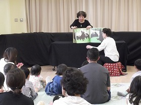 大型絵本の読み聞かせをしている女性2人と聞いている親子