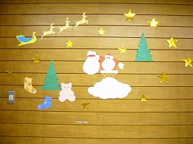 画用紙や折り紙で作ったサンタクロース、クリスマスツリーの下にいるくまと靴下の装飾。