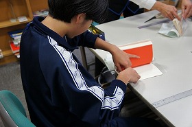 職業体験に来た中学生が、本のブックカバー貼り体験を行っている画像です。